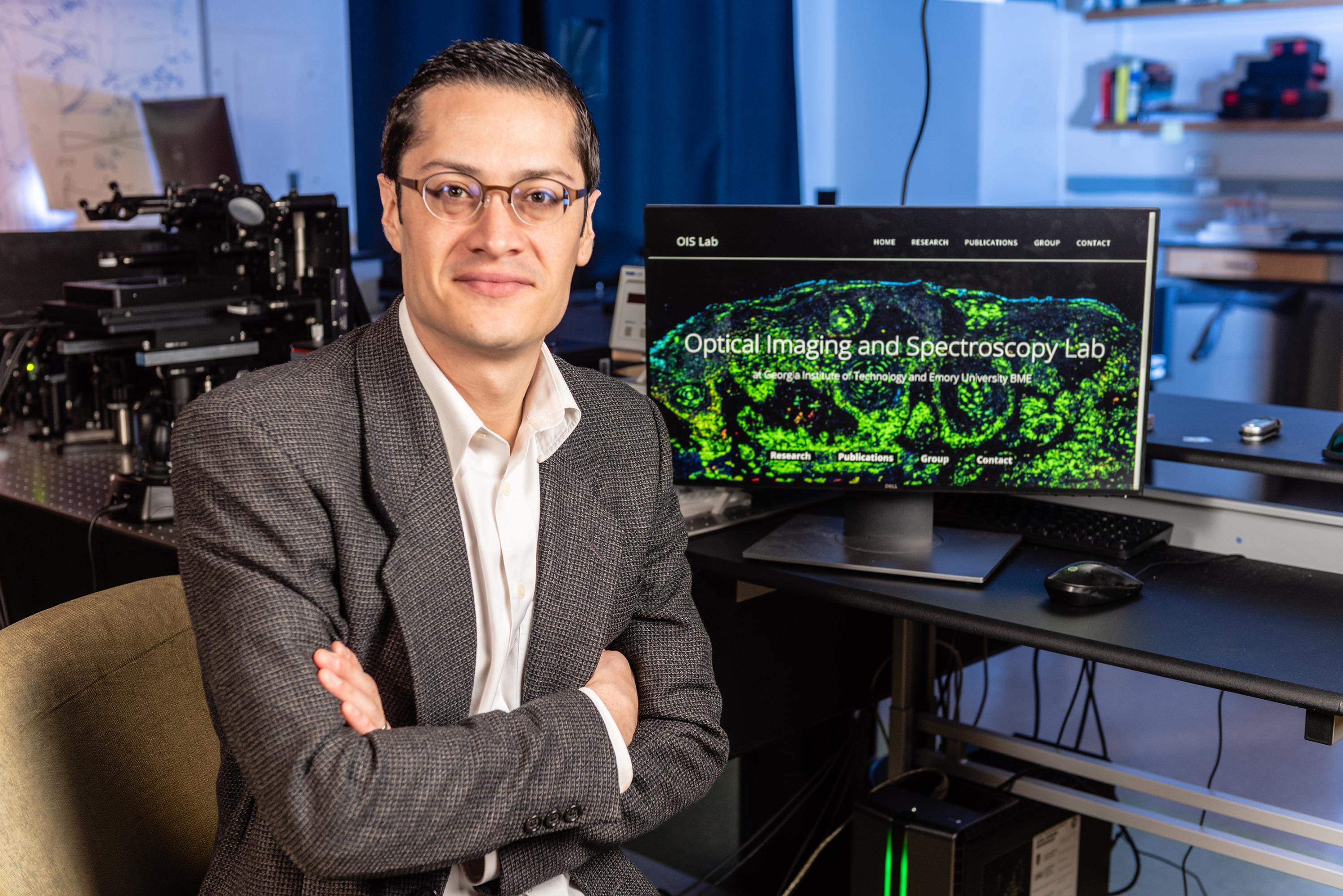 Dr. Francisco Robles, chief science officer of Cellia Science, Inc., sits at his desk in his lab at Georgia Tech. On the desk is a computer monitor with the words Optical Imaging and Spectroscopy Lab displayed.  