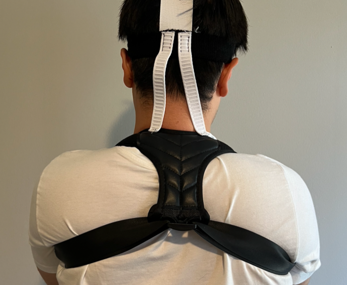 A person from behind with head upright wearing a black shoulder harness starting at the base of the back of the neck and looping under each arm. Two white straps connect the harness to a black headband.