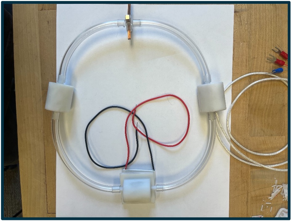 Large loop of plastic tubing with a black wire and a red wire in small loops inside the larger loop