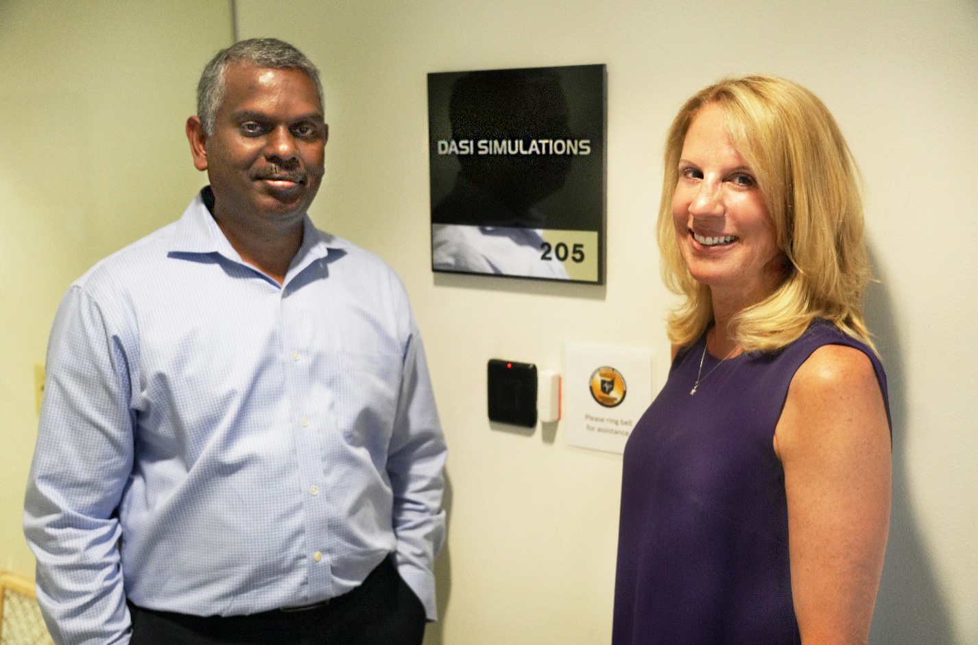 Company founders stand on either side of a sign indicating the offices of DASI Simulations. 